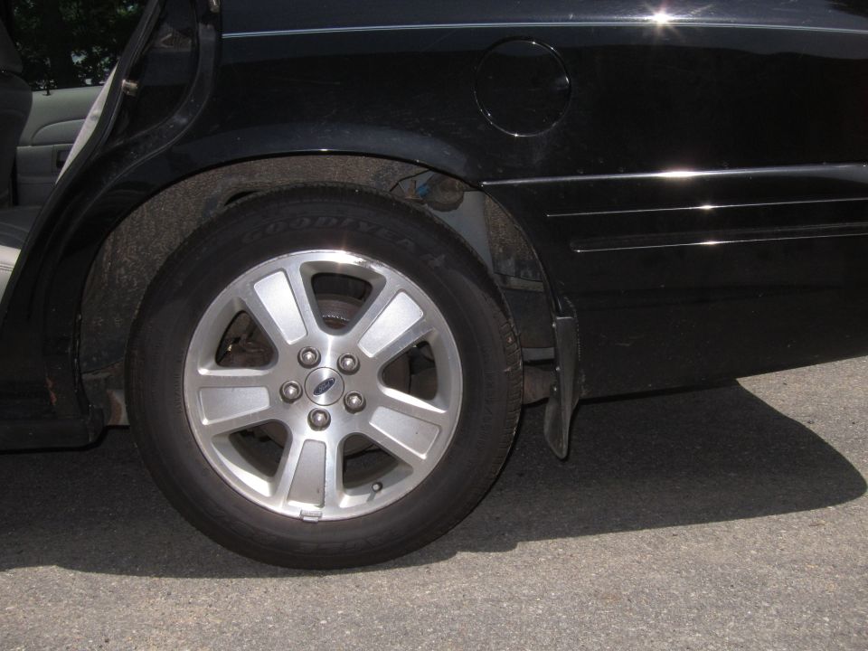 Black 2001 Ford Crown Victoria rear wheel and fender, showing a silver five-spoke rim with a Ford logo