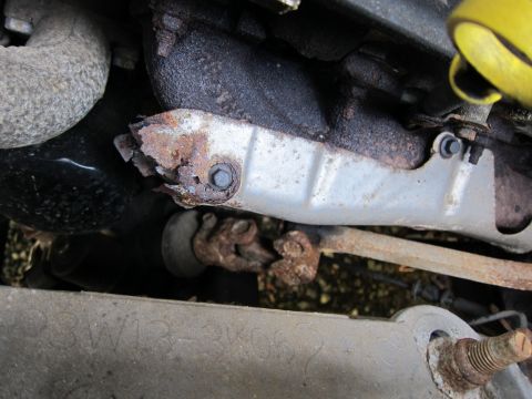 2001 Ford Crown Victoria - Close-up view of a corroded exhaust manifold and associated engine components, showing significant rust and wear.
