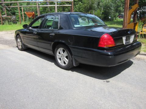 2001 Ford Crown Victoria - This black 2001 Ford Crown Victoria is shown from the rear quarter angle, parked outdoors with some machinery in the background.