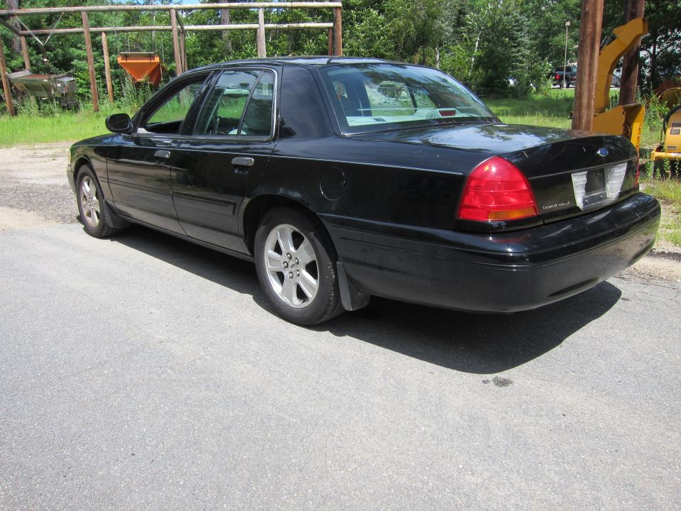 Black 2001 Ford Crown Victoria parked on asphalt, rear quarter view. Some construction equipment is visible in the background
