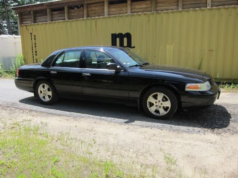 2001 Ford Crown Victoria - A black sedan is parked on a gravel surface beside a large yellow shipping container.