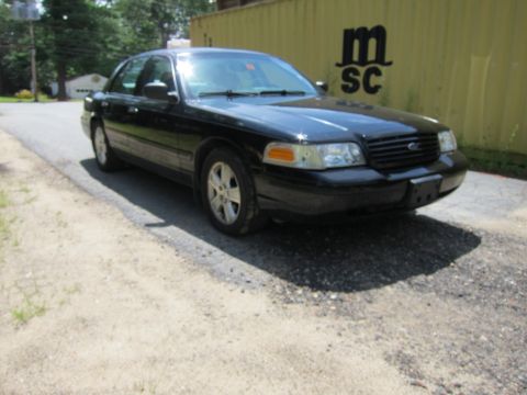 2001 Ford Crown Victoria - A black 2001 Ford Crown Victoria is parked on a gravel surface with a yellow shipping container in the background.