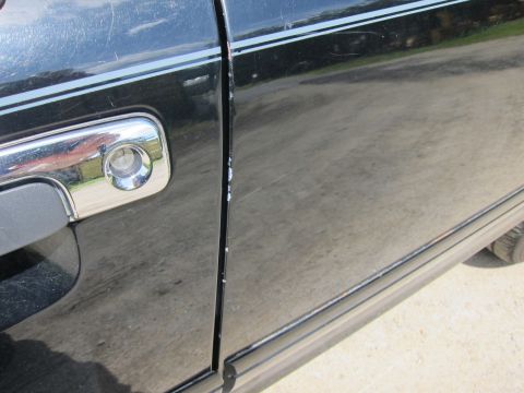 2001 Ford Crown Victoria - The side panel of a black vehicle shows minor paint damage near the door seam and a chrome door handle.