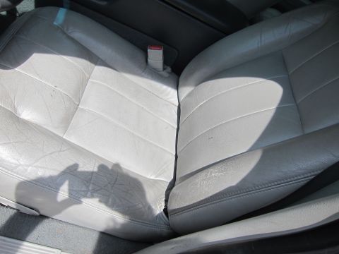 2001 Ford Crown Victoria - The interior of a car shows worn light gray leather seats and a seatbelt.