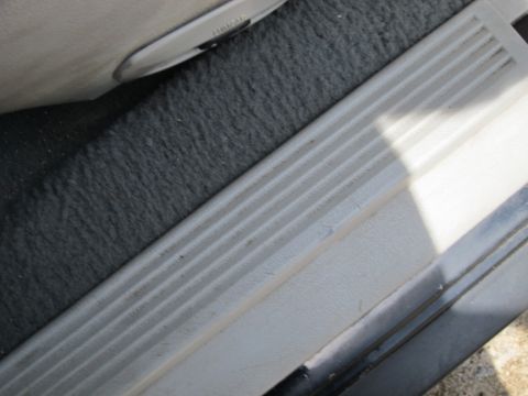 2001 Ford Crown Victoria - The interior door sill of a vehicle shows wear and tear with textured plastic trim and dark carpeting.