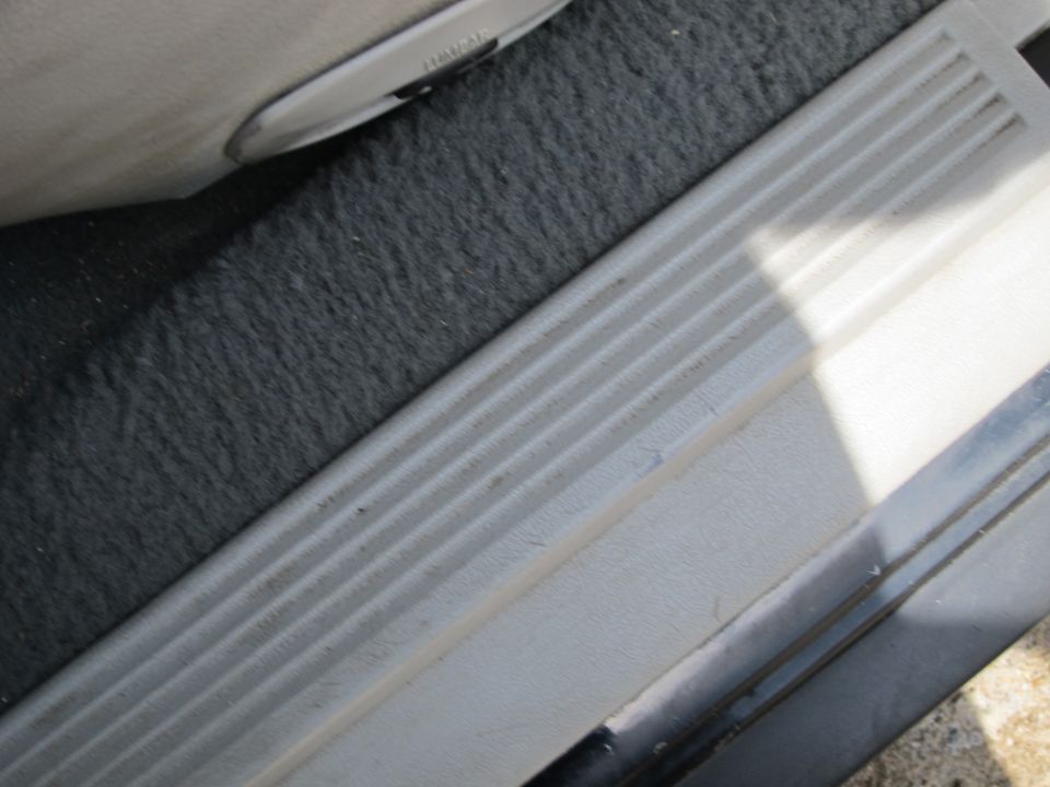Close-up of a car's interior door sill with textured plastic and carpet