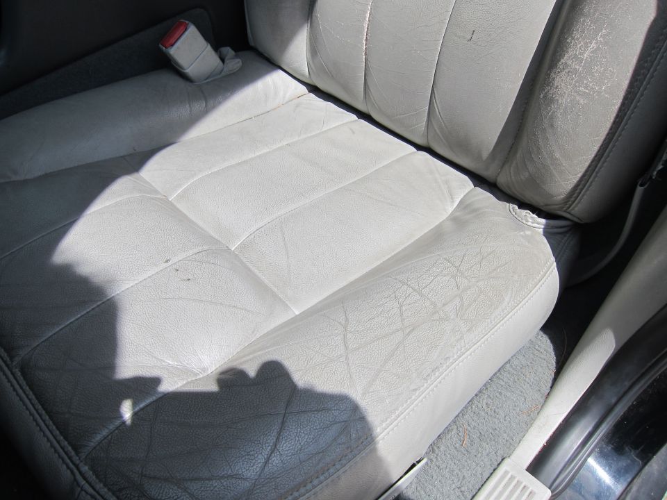 Close-up of worn light gray leather car seats and seatbelt