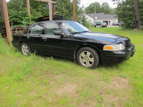 2001 Ford Crown Victoria - Black 2001 Ford Crown Victoria sits in a grassy area with trees and a building in the background.
