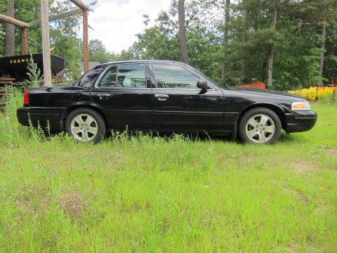 2001 Ford Crown Victoria - A black 2001 Ford Crown Victoria is parked on a grassy area with trees in the background.