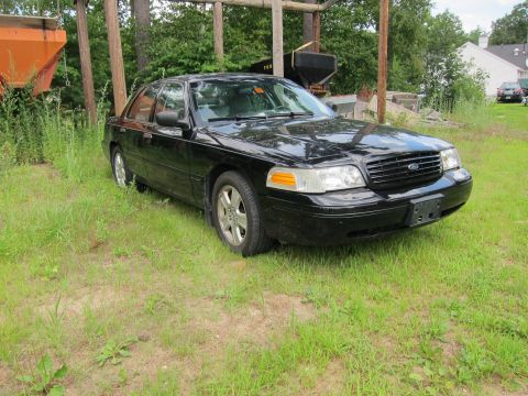 2001 Ford Crown Victoria - A black 2001 Ford Crown Victoria is parked in a grassy area with trees and buildings in the background.
