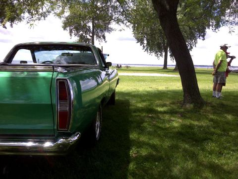 1971 Ford Ranchero - A green 1971 Ford Ranchero is seen from the rear, parked in a grassy area with trees and a lake in the background.