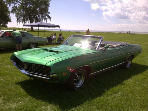 1971 Ford Ranchero - A green convertible with a distinctive hood scoop sits on a grassy field near a body of water.