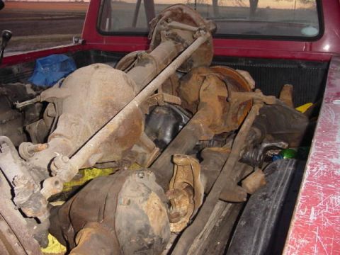1992 Ford Bronco - Several rusty rear axles are piled in the bed of a red pickup truck.