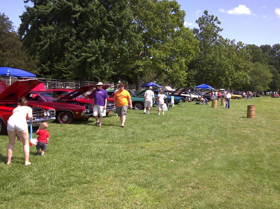 People milling around a car show with many vehicles on display under tents and in the open