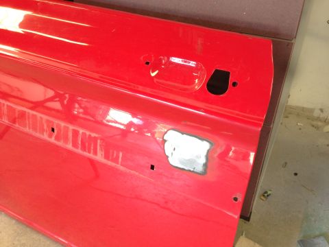 1964 Ford Fairlane - Close-up of a red car door showing a patch of primer and the cutout for the door handle.