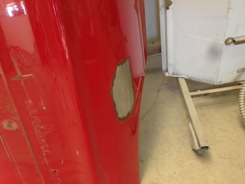 1964 Ford Fairlane - Close-up of a red car fender with a patch of primer, indicating repair work.