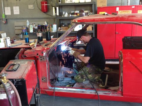 1964 Ford Fairlane - A mechanic works on the interior of a red 1964 Ford Fairlane, welding metal.