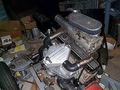 1976 Ford Bronco - Engine assembly with a prominent supercharger and air filter sits amidst garage clutter.