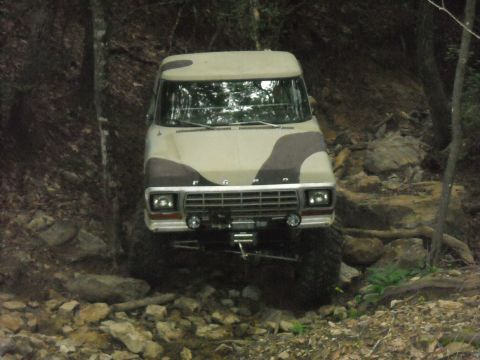1979 Ford F-150 - This Ford F-150 is navigating a challenging, wooded terrain with large rocks and uneven ground.