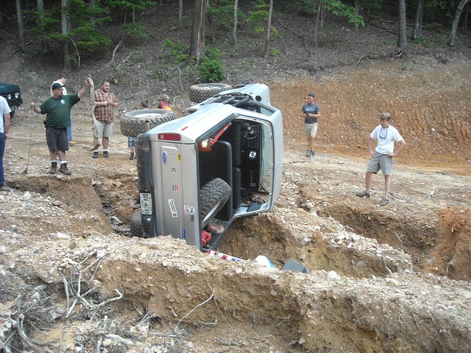 Silver 1979 Ford F-150 on its side in a ditch with people around