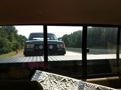 1989 Ford Bronco - A green Ford F-Series truck is being transported on a trailer, viewed from the rear window.