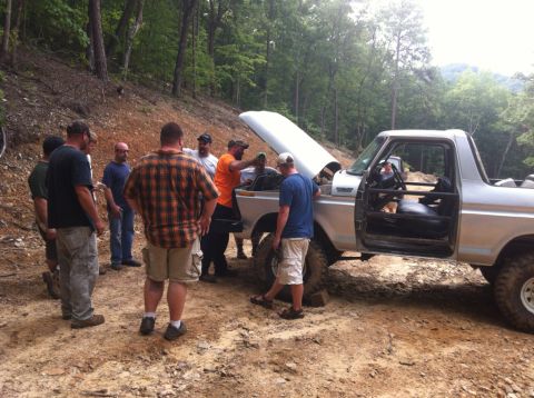 1989 Ford Bronco - A group of men inspect a silver 1989 Ford Bronco with its hood up, parked on a dirt trail.