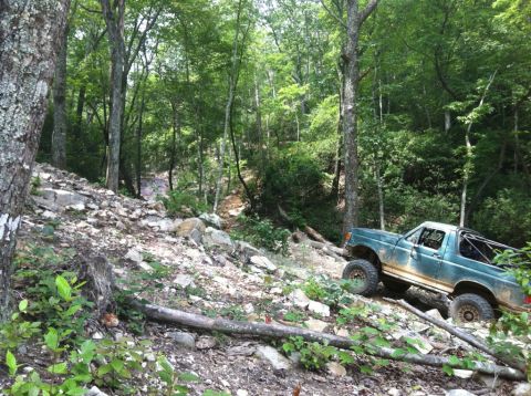 1989 Ford Bronco - A 1989 Ford Bronco navigates a challenging off-road course through a dense forest.