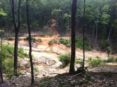 1989 Ford Bronco - A muddy construction site with tire tracks is visible on a hill surrounded by trees.
