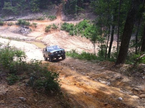 1989 Ford Bronco - A 1989 Ford Bronco navigates a challenging off-road course with steep inclines and muddy patches.
