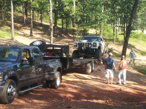 2013 Ford Bronco - A lifted Ford Bronco is transported on a trailer by a dark pickup truck through a wooded area.