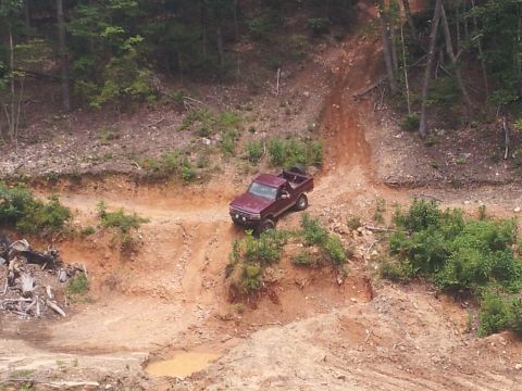 2013 Ford Bronco - A maroon pickup truck navigates a challenging off-road trail with steep inclines and loose dirt.