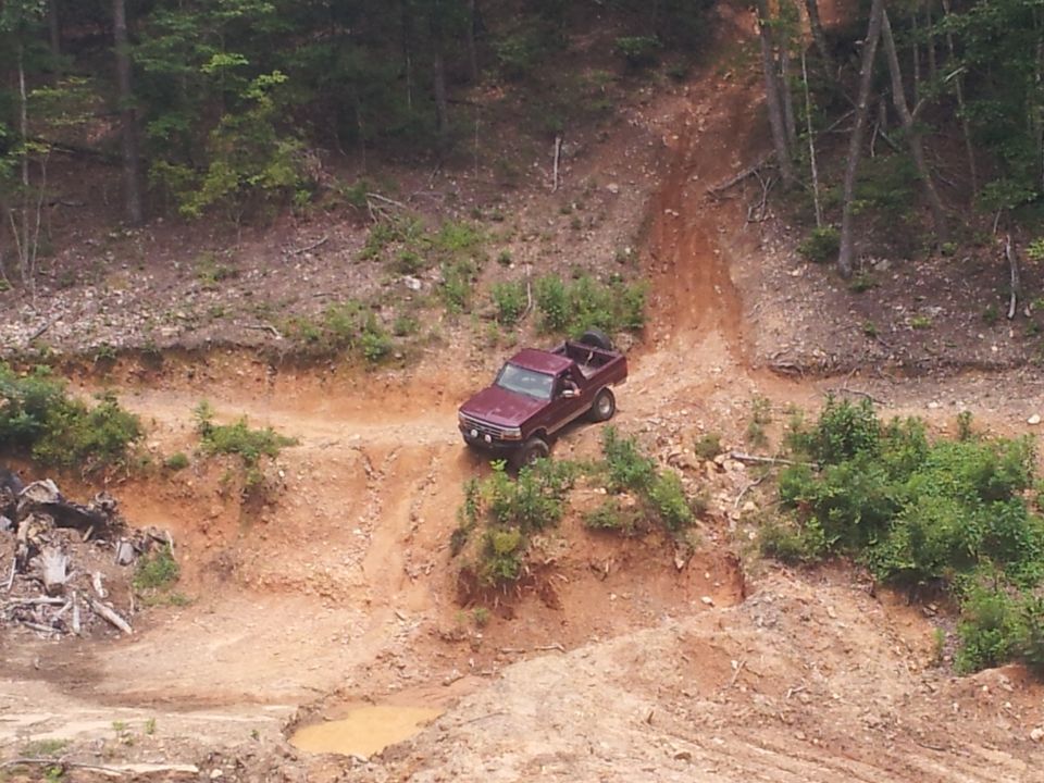 Maroon pickup truck driving down a steep dirt hill with trees on either side