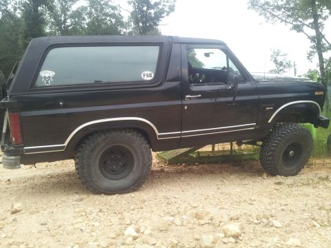 2013 Ford Bronco - This black SUV, likely from the 1980s based on its body style, is shown from the side with a lifted suspension and off-road tires.
