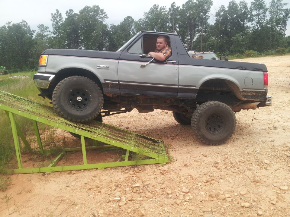 Ford Bronco with lifted suspension and large tires climbing a green metal ramp
