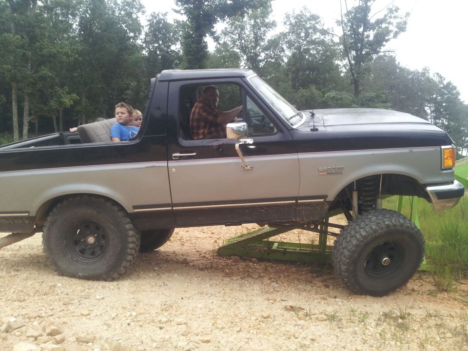 Side view of a lifted, two-tone pickup truck with people in the cab and bed