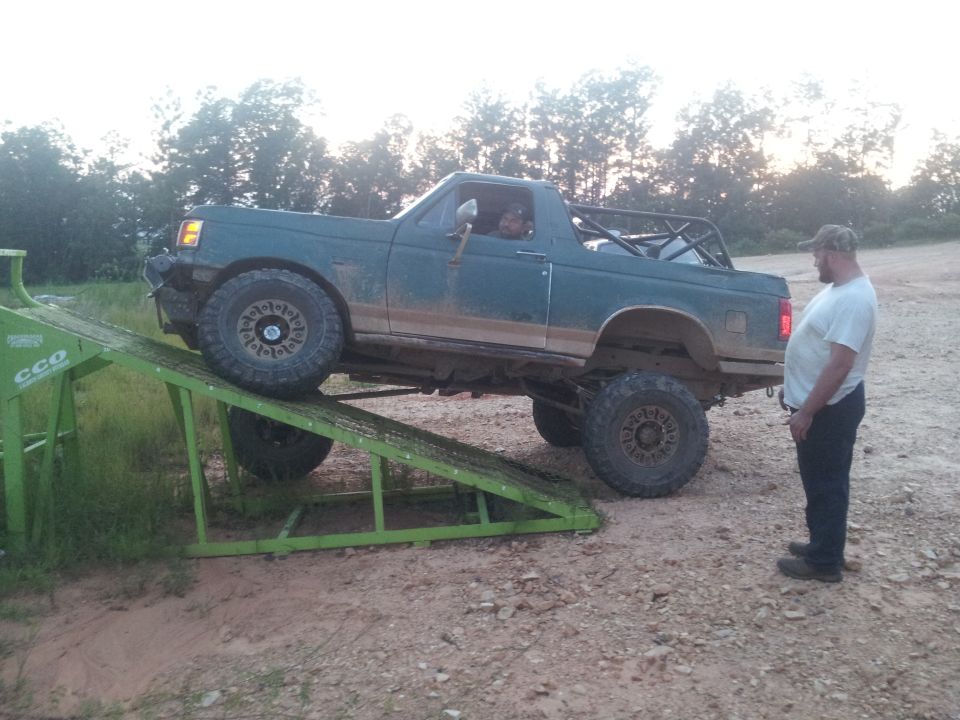 Green Ford Bronco with roll cage on a green ramp, front right tire elevated