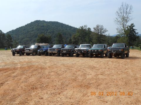 2013 Ford Bronco - Several off-road vehicles are lined up on a dirt lot, with a wooded hill visible behind them.