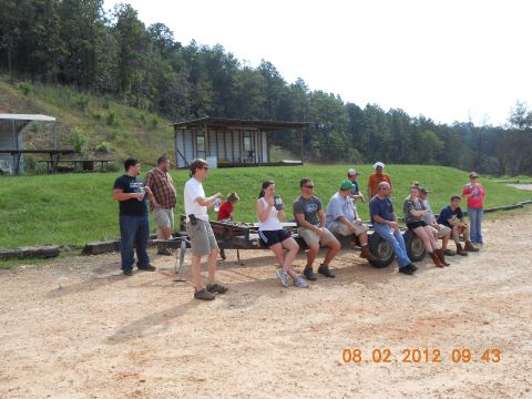 2013 Ford Bronco - A group of people are gathered outdoors, sitting on a trailer with a building and wooded area behind them.