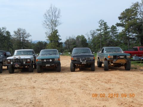 2013 Ford Bronco - Several off-road trucks are lined up in a dirt area with trees in the background.