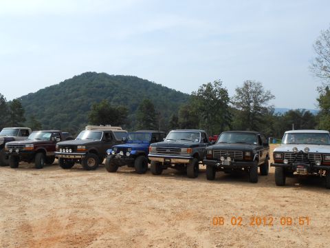 2013 Ford Bronco - A collection of older model Ford trucks and SUVs are lined up on a dirt lot.