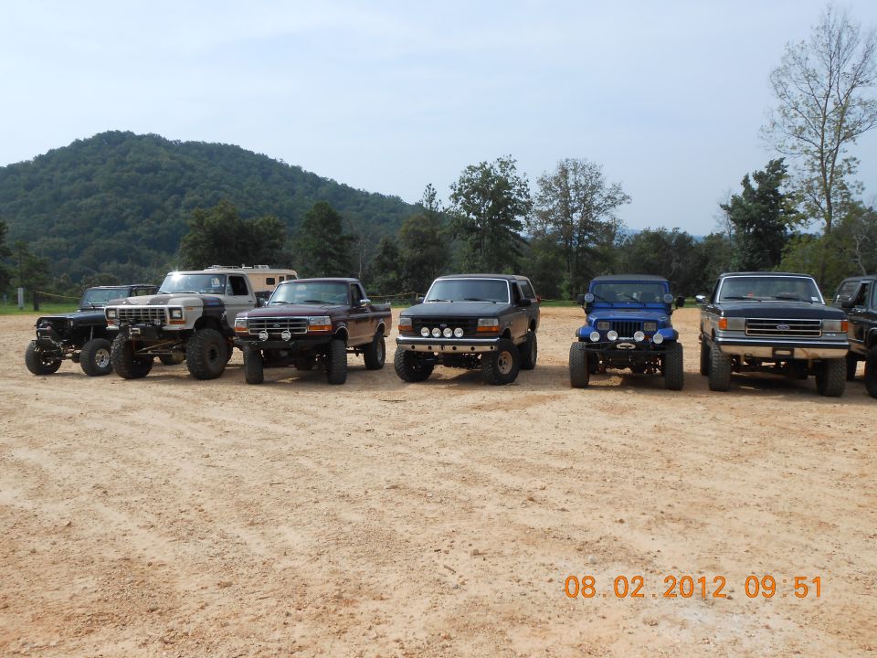 Dark blue 1992 Ford Bronco with aftermarket lights parked in a line of off-road vehicles