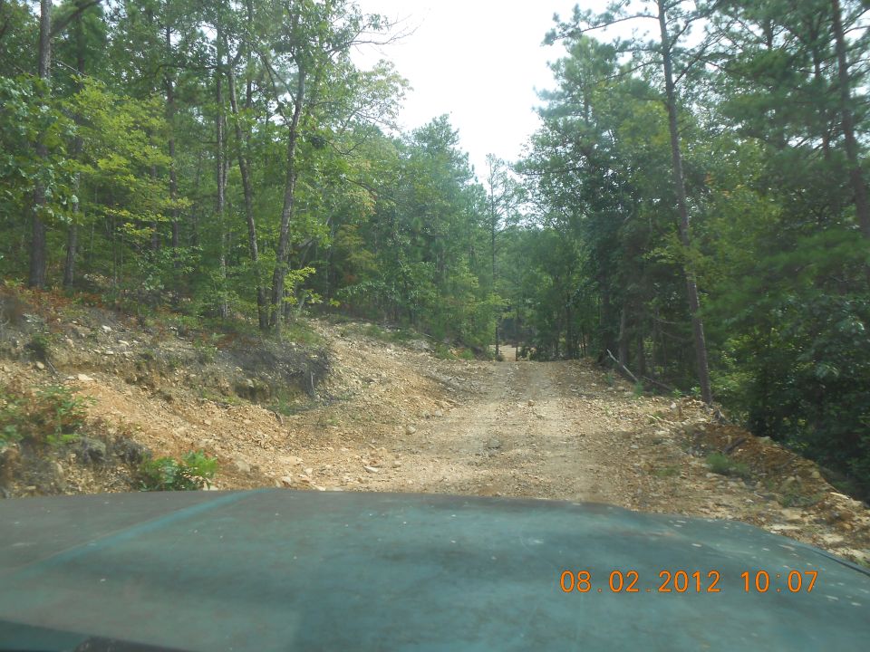 view from inside a vehicle looking down a rough dirt road in a wooded area. Timestamp reads 08 02 2012