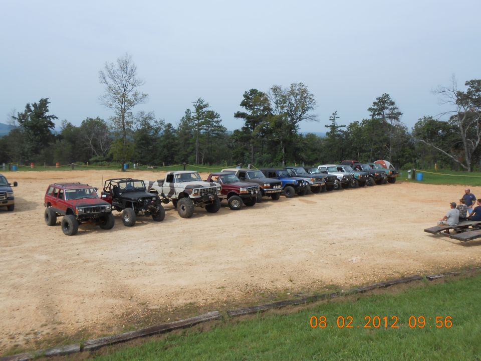 Line of modified off-road SUVs and trucks parked on dirt, side view