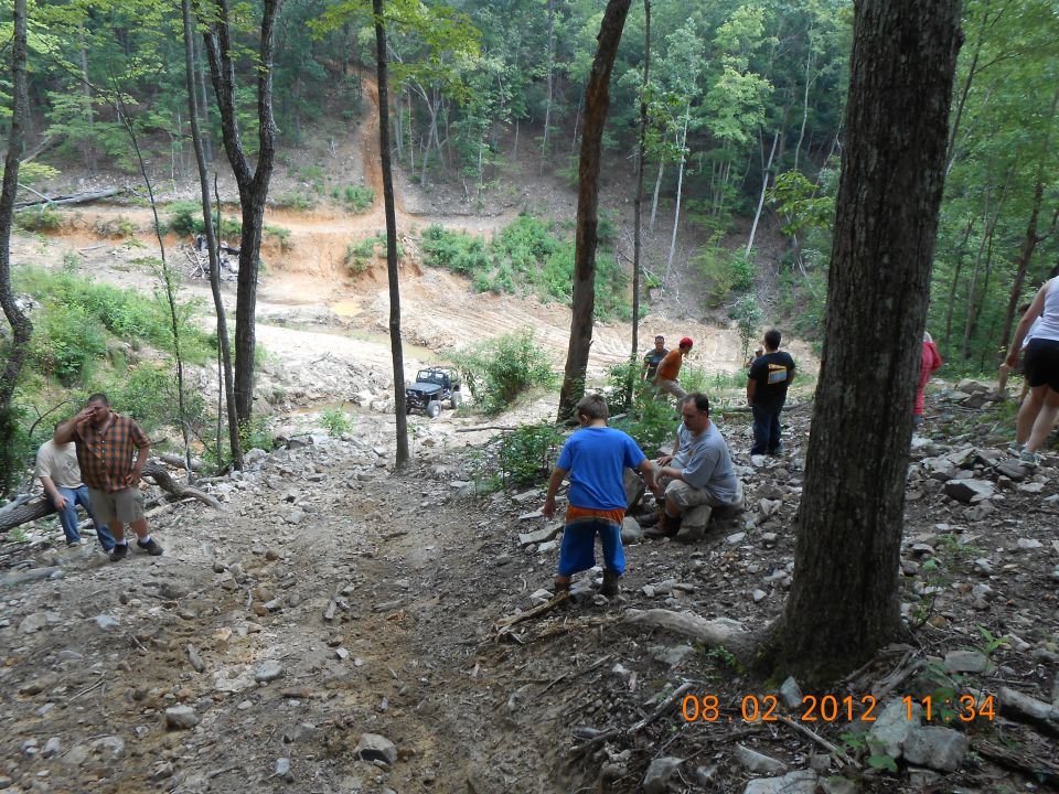 People gathered on a rocky trail with a Jeep driving up a dirt path in the background