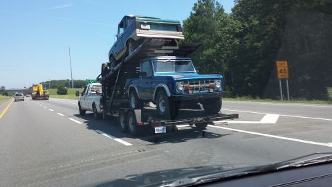 1987 Ford Bronco - Two Ford Broncos are transported on a car hauler on the highway.
