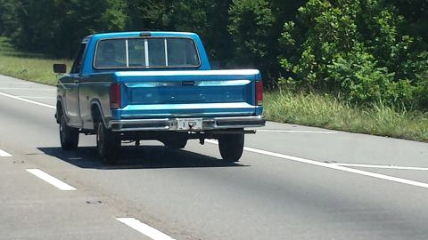 1987 Ford Bronco - A blue pickup truck from the 1980s is seen driving on a highway.
