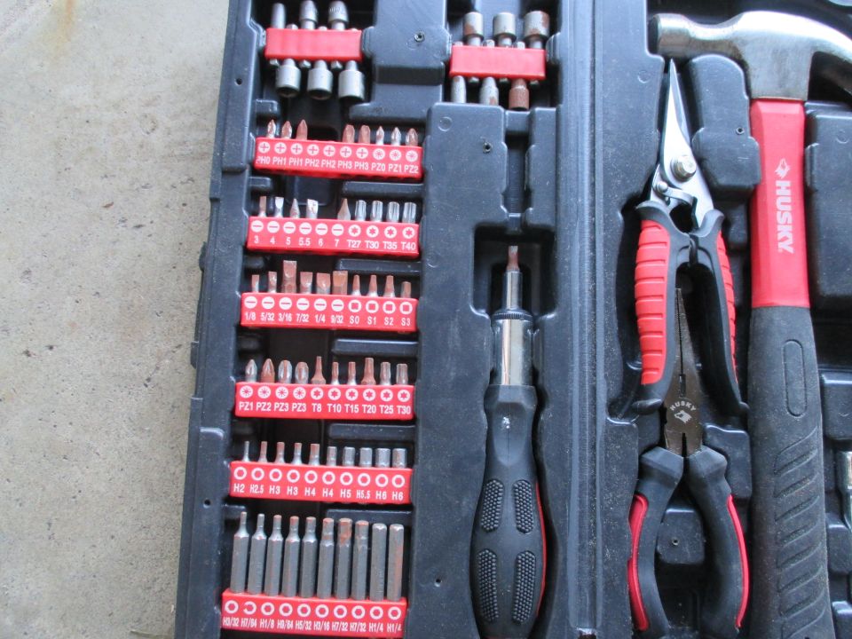 Tool kit containing various screwdriver bits, a multi-bit screwdriver, pliers, and a hammer. Text on bits indicates sizes like PH2, T20, and H4