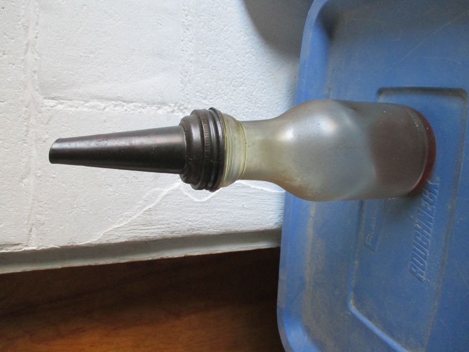 Oil can with metal spout and translucent body, resting on a blue plastic container with "ROUGHNECK" text