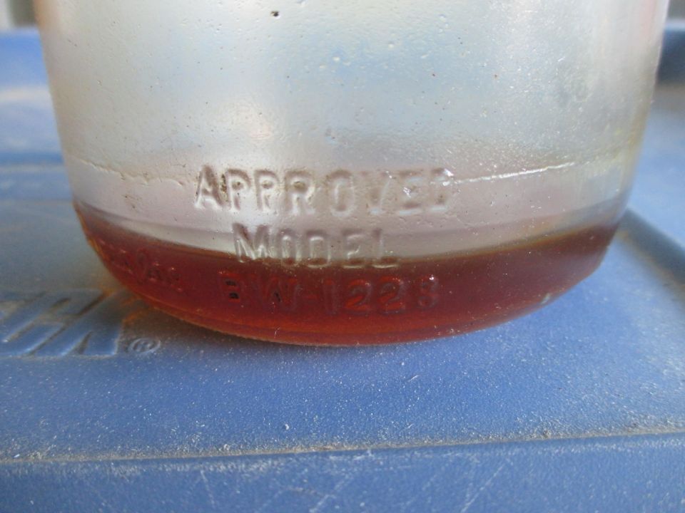Glass jar with amber liquid and embossed text 'APPROVED MODEL BM1223'