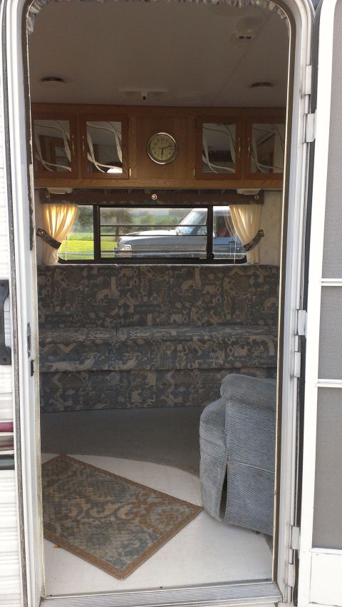 1995 Ford Bronco - View from outside an RV shows the interior, including a couch and cabinets, with a vehicle seen through the window.